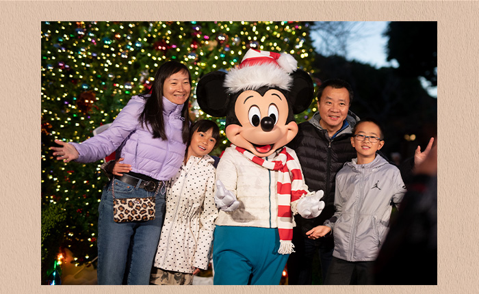 A family of four taking a picture with Mickey Mouse. Behind them a huge Christmas tree finely decorated