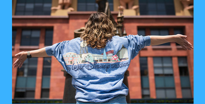 An image capturing a fan with her arms spread apart she is wearing a Walt Disney Studios sweater.
