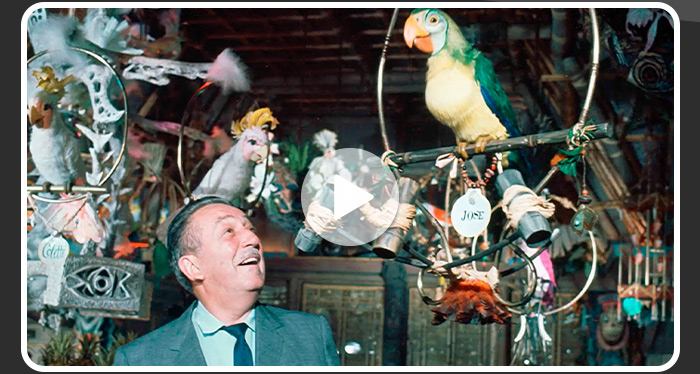Walt Disney smiles up at Jose the Tiki Room parrot amid tropical animatronic birds.