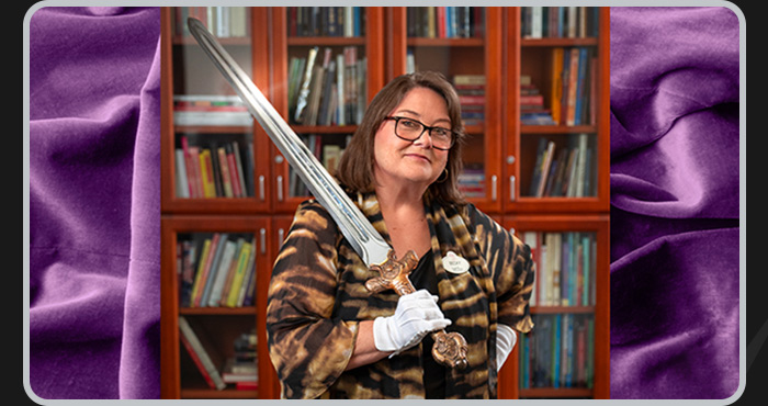Walt Disney curator holds a gleaming prop sword while wearing white gloves in the reference library.