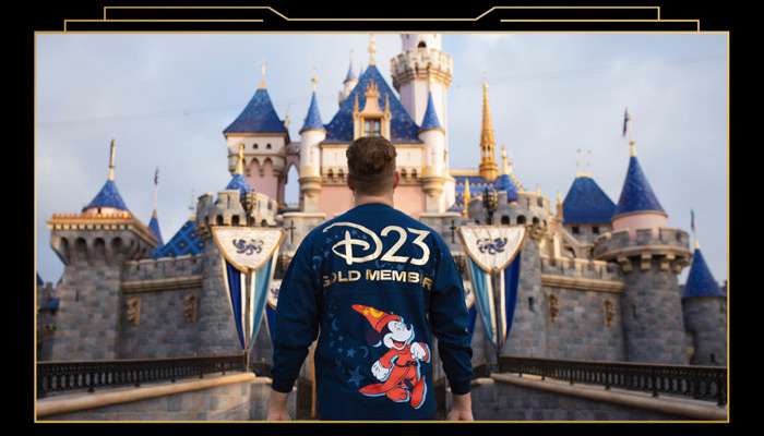 Guest wearing D23 Gold Member jacket featuring sorcerer Mickey standing in front of Sleeping Beauty Castle.