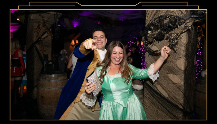 Two  guests dressed in Disney-inspired costumes dance and laugh at a D23 Halloween event.