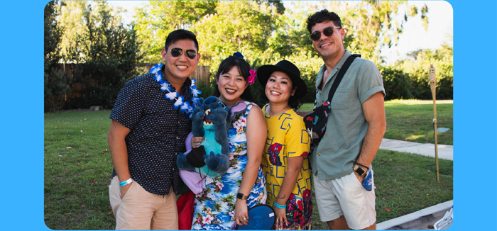 Four friends outside, smiling with leis while holding a plush Stitch
