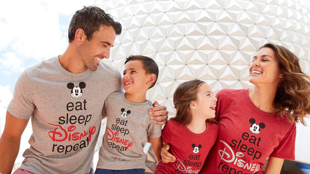 A family of four wearing Disney t-shirts that read, 'Eat Sleep Disney Repeat' they are lovingly embracing their child as they smile.