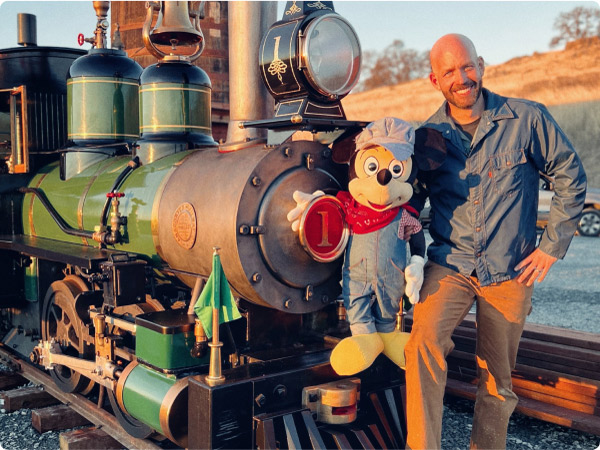 Bret Iwan and Mickey Mouse taking a picture on the tracks while talking trains and Christmas.
