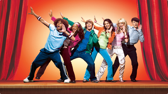 High School Musical featuring the entire cast. From left to right is Corbin Bleu, Monique Coleman, Zac Efron, Vanessa Hudgens, Ashley Tisdale, and Lucas Grabeel  all while in front of a red theater curtain.