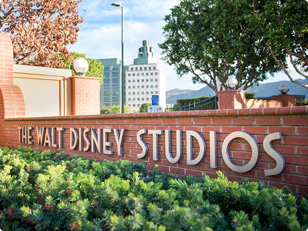 The Walt Disney Studio entrance sign. Large metallic letters on a red brick wall, surrounded by greenery and a cityscape.