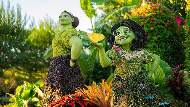 Encanto topiary display of Luisa and Miracle. Greenery sculptures of the Madrigal sisters surrounded by colorful flowers.