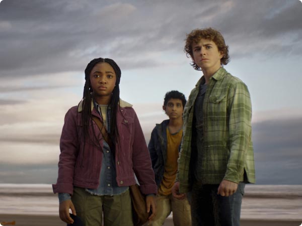 Percy, Annabeth, and Grover from Percy Jackson and the Olympians stand on a cloudy beach, looking onward with determined expressions.
