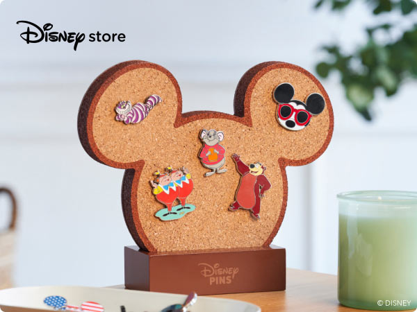 Mickey-shaped cork board displaying Disney pins-Cheshire cat, Tweedle Dee and Dum, Timothy Mouse, Baymax, and Mickey with red sunglasses.