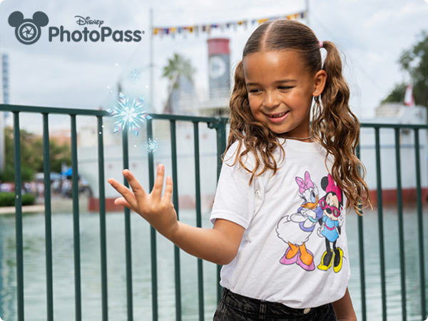 Disney PhotoPass Magic shot-smiling girl in Minnie-and-Daisy tee admires a sparkling effect above her hand.
