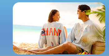 Beach duo in grey spirit jerseys; the woman's back spells big red “OHANA.”