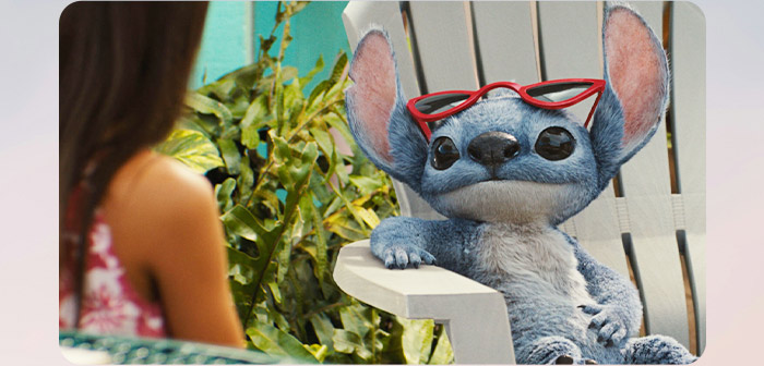 Chill Stitch lounges in a patio chair wearing red sunglasses,  chatting with a woman off-camera