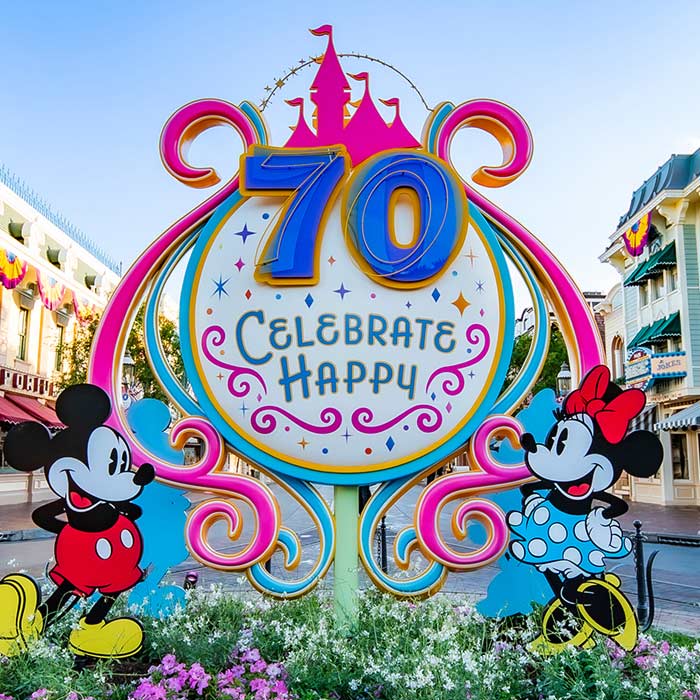 Main-Street sign reads “70 Celebrate Happy,” with smiling Mickey (left) and Minnie (right) beneath swirling pink-and-gold castle flourishes.