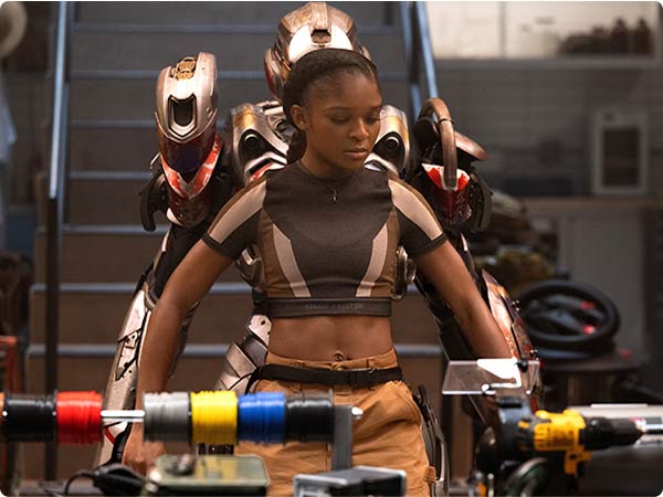 Riri Williams (Ironheart) tested a bronze-and-black prototype suit in her workshop, flanked by two unfinished armored exosuits.