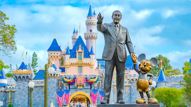 Partners statue of Walt Disney and Mickey before bunting-lined Sleeping Beauty Castle under a bright summer sky.