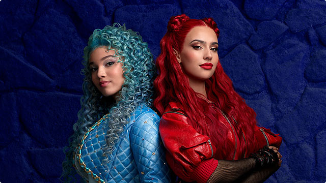 Chloe and Red from Descendants: The Rise of Red pose back to back in red and blue outfits against dark stone wall.