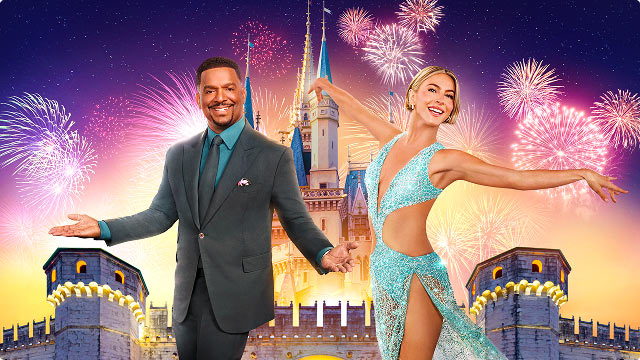 Hosts Alfonso Ribeiro and Julianne Hough posing in front of Disney castle with fireworks in the sky.