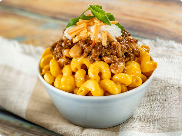 Impossible® Chili Cheese Macaroni and Cheese from the EPCOT International Food & Wine Festival served in a small, white bowl placed on top of a brown and white towel on a wooden countertop.