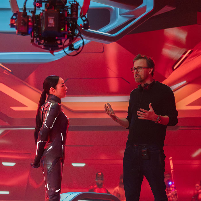Behind the scenes of Tron: Ares with actress in suit speaking to director Joachim Ronning on a futuristic red-lit set.