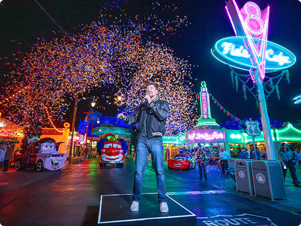 Performer sings amid confetti and neon lights on Route 66 in Cars Land at Disney California Adventure.
