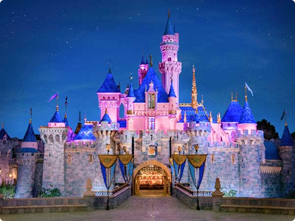 Sleeping Beauty Castle at Disneyland illuminated at night with blue and gold holiday decor.