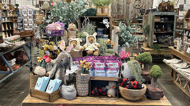 Spring home decor display featuring plush bunnies, floral arrangements, tulips, greenery, and decorative accents inside a rustic shop.