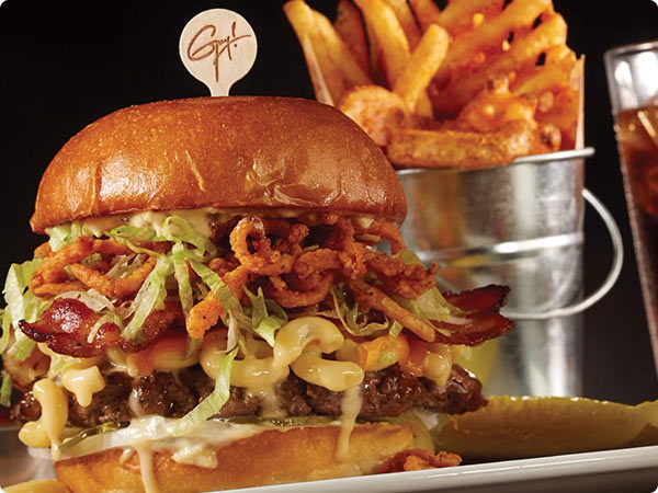 Loaded gourmet burgers topped with bacon, crispy onions, and melted cheese, served with fries in a metal cup.